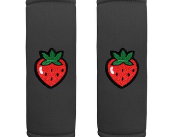 May include: Two gray seatbelt covers with embroidered strawberry designs. The strawberries are red with green leaves.