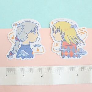 Może przedstawiać: Dwie naklejki z ilustracjami w stylu anime postaci z profilu. Jedna ma srebrne włosy w warkoczu, nosi niebieską sukienkę, a druga ma blond włosy, nosi czerwono-pomarańczowy str&oacute;j. Obie mają akcenty chmur i ognia.