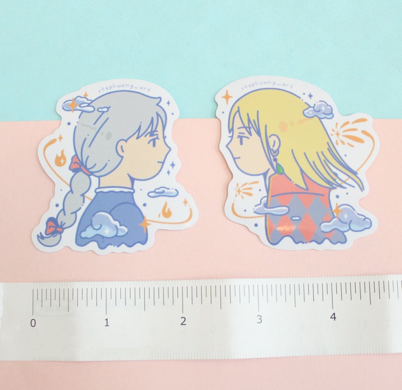 Może przedstawiać: Dwie naklejki z ilustracjami w stylu anime postaci z profilu. Jedna ma srebrne włosy w warkoczu, nosi niebieską sukienkę, a druga ma blond włosy, nosi czerwono-pomarańczowy str&oacute;j. Obie mają akcenty chmur i ognia.