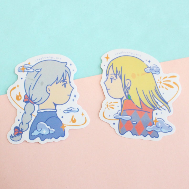 Może przedstawiać: Dwie naklejki z ilustracjami postaci z kresk&oacute;wek w profilu. Jedna ma szare włosy w warkoczu, w niebieskiej sukience. Druga ma blond włosy i czerwono-pomarańczowy top we wzory. Oba mają akcenty chmur i ognia.