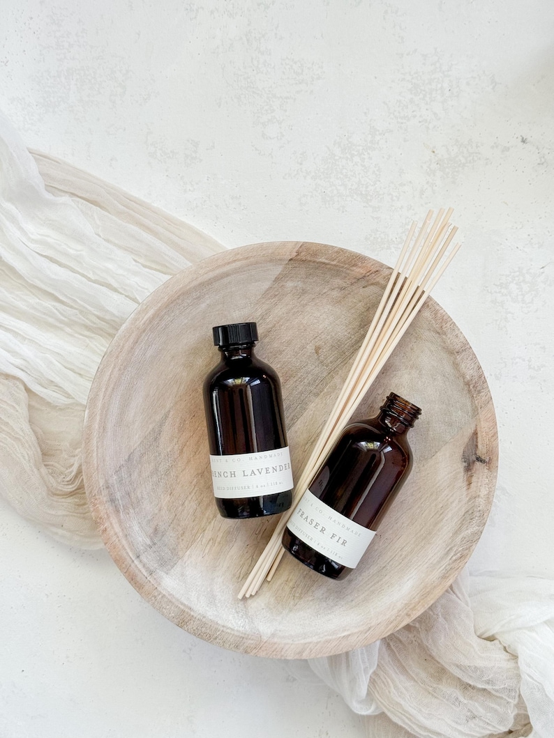 May include: Two brown glass bottles with white labels in a wooden bowl. The labels read "French Lavender" and "Fraser Fir".  Wooden sticks are in the bowl.