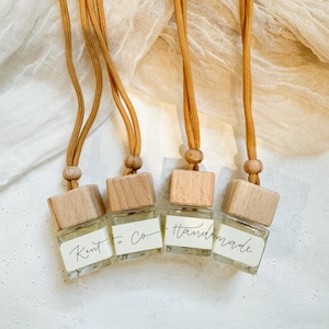 May include: Four small glass bottles with wooden tops and brown string hangers. The bottles are filled with a clear liquid and have handwritten labels that say "Kent + Co." and "Handmade".