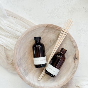May include: Two brown glass bottles with white labels in a wooden bowl. The labels read "French Lavender" and "Fraser Fir".  Wooden sticks are in the bowl.