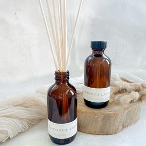 May include: Two brown glass bottles with black lids and white labels. The bottles are filled with a clear liquid and have reeds sticking out of the top. The labels read "Coconut Lemon" and "French Lavender".