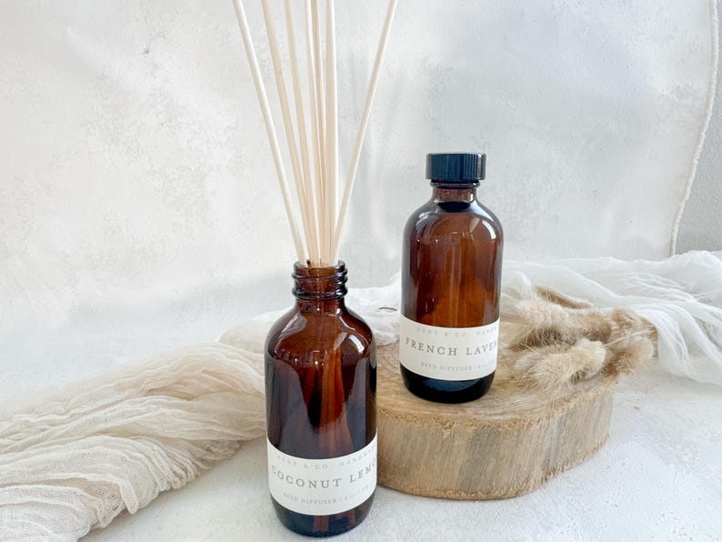 May include: Two brown glass bottles with black lids and white labels. The bottles are filled with a clear liquid and have reeds sticking out of the top. The labels read "Coconut Lemon" and "French Lavender".