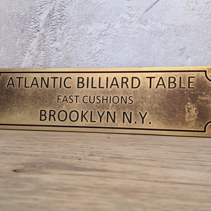 Personalized brass metal sign for a billiard table, made from solid brass that has been aged so as to develop the antique patina