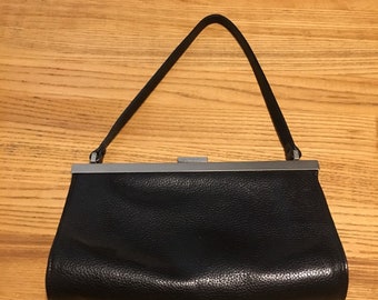 Könnte beinhalten: Eine schwarze Leder-Clutch mit einem silbernen Verschluss und einem dünnen Schulterriemen.