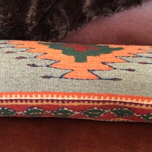 May include: A gray and orange patterned throw pillow with a geometric design. The pillow is made of woven fabric and has a fringe border.