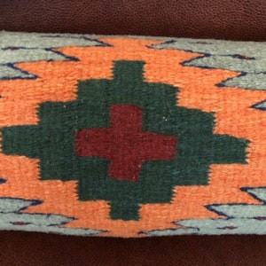 May include: A decorative pillow with a geometric pattern in shades of orange, green, and red. The pillow is made of woven fabric and has a fringed edge.