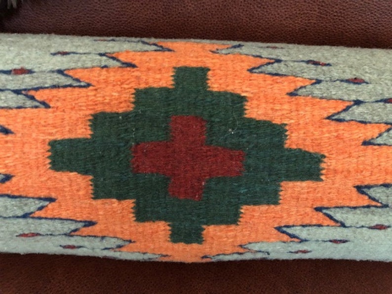 May include: A decorative pillow with a geometric pattern in shades of orange, green, and red. The pillow is made of woven fabric and has a fringed edge.
