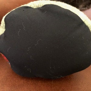 May include: A round, multi-colored pillow with a black fabric bottom. The pillow has a green, orange, and red pattern.
