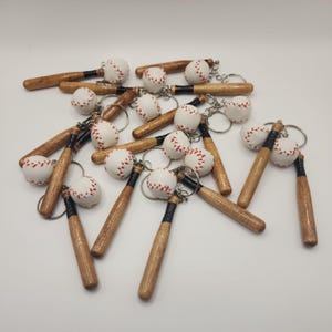 May include: A collection of baseball keychains, each featuring a miniature wooden baseball bat with a black handle and a white baseball with red stitching attached by a silver metal keyring. The bats have a natural wood grain finish.