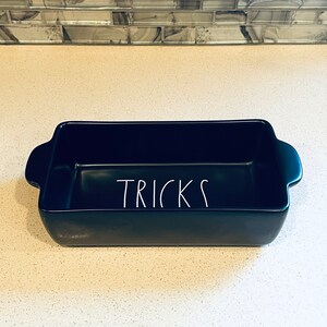 May include: A black ceramic baking dish with the word "TRICKS" written in white on the front.