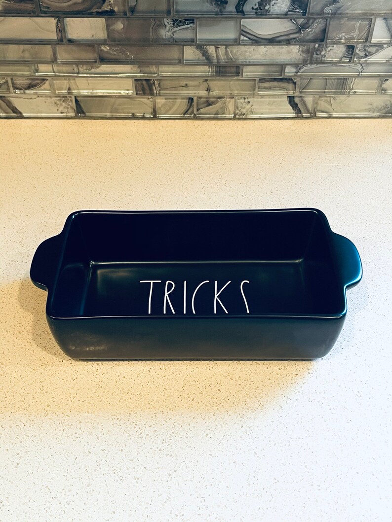 May include: A black ceramic baking dish with the word "TRICKS" written in white on the front.