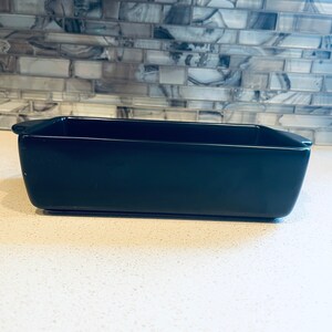 May include: A black rectangular ceramic baking dish with rounded edges and two small handles on the sides.