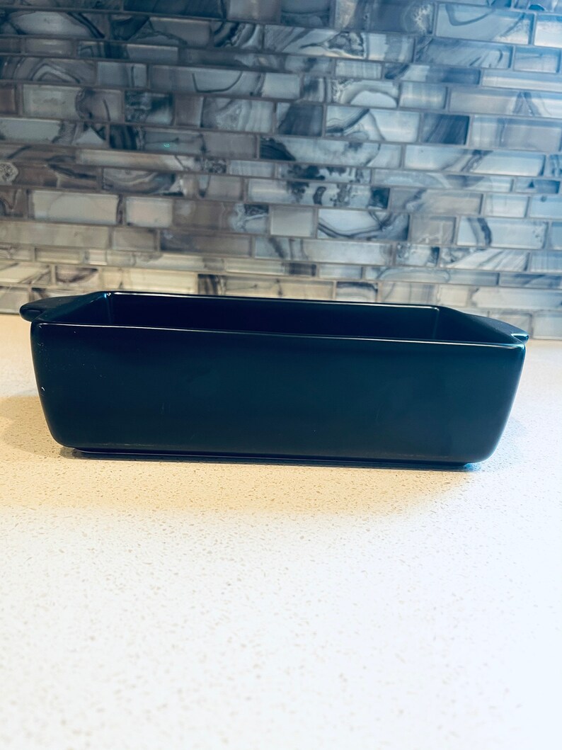 May include: A black rectangular ceramic baking dish with rounded edges and two small handles on the sides.