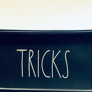 May include: Black ceramic dish with the word "TRICKS" written in white on the front.