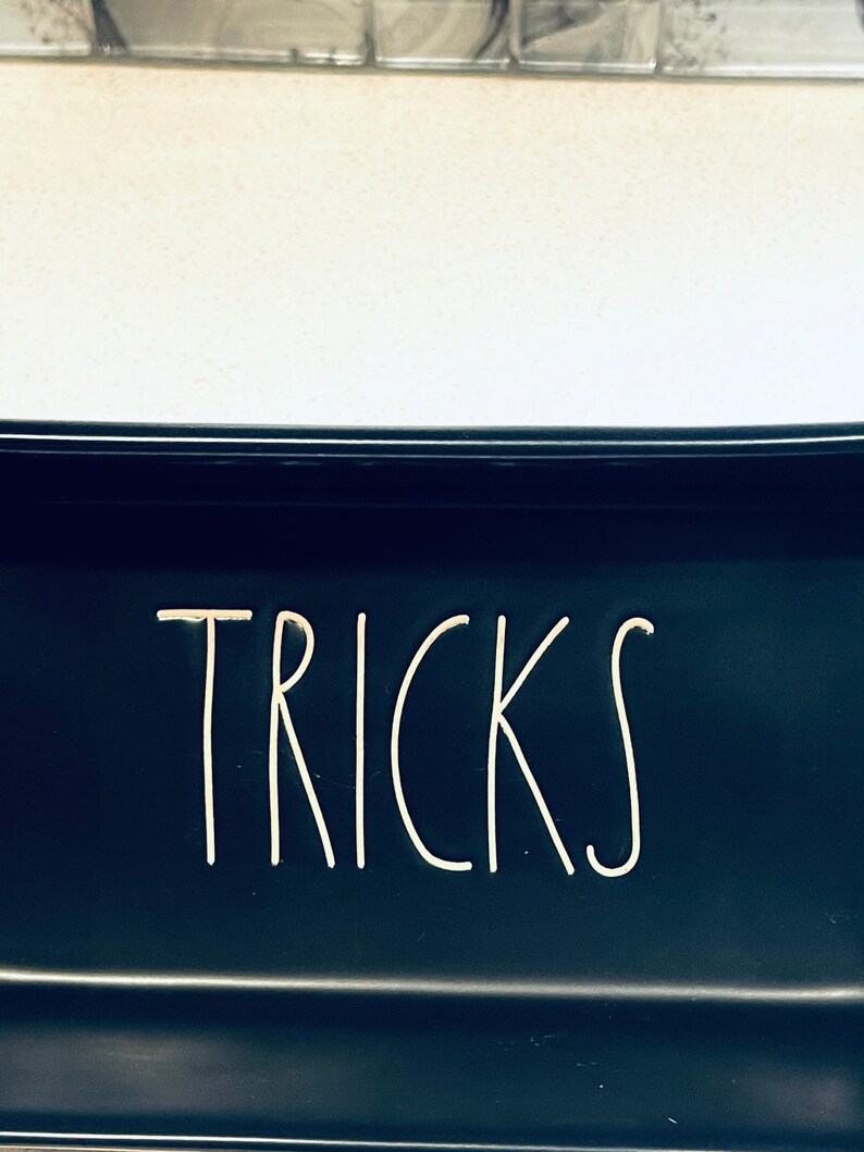 May include: Black ceramic dish with the word "TRICKS" written in white on the front.