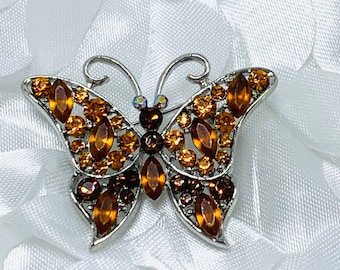 Puede incluir: Un broche de mariposa de plata con diamantes de imitación marrones y ámbar.