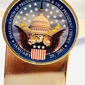 Pode incluir: Marca-páginas dourado com um medalhão redondo azul e dourado que representa o edifício do Capitólio dos Estados Unidos, uma águia e o texto "Inauguration of President Bush & Vice President Cheney January 20, 2001".