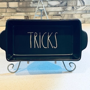 May include: Black rectangular baking dish with white lettering that says "TRICKS" on a metal stand.