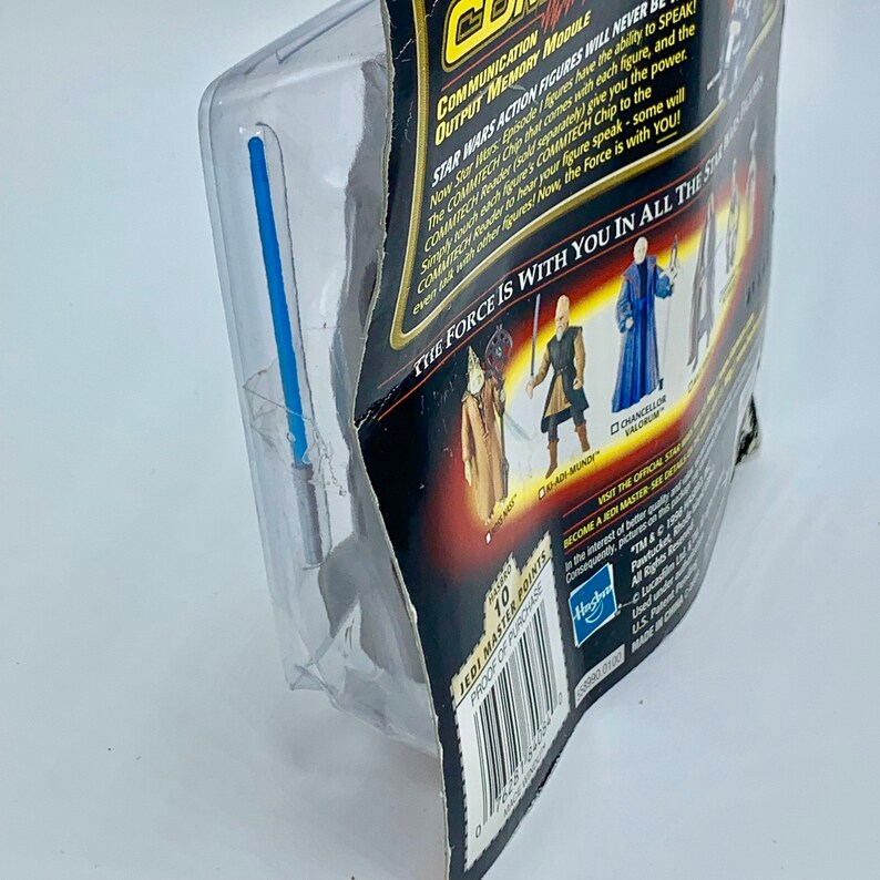 May include: A Star Wars action figure packaging featuring a black and silver background with a blue lightsaber. The packaging includes a communication output memory module and a Jedi Master Points card. The text on the packaging reads "The Force is with you in all the stories."
