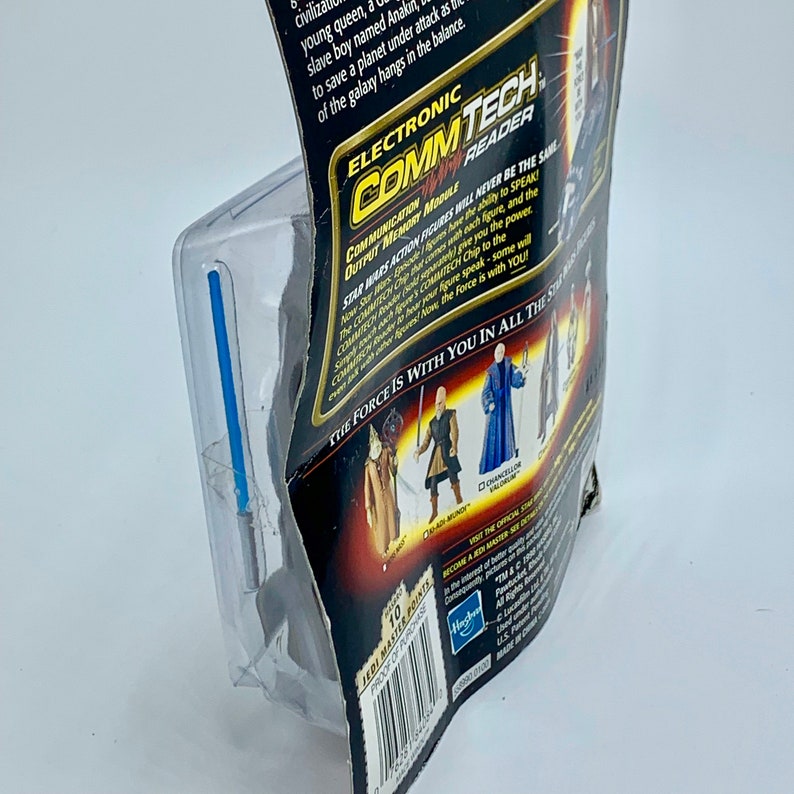 May include: A Star Wars action figure packaging featuring a blue lightsaber, a black background, and the text "Electronic CommTech Communication Reader Output Memory Module". The packaging also features images of various Star Wars characters, including a Jedi Master, a Sith Lord, and a Chancellor.