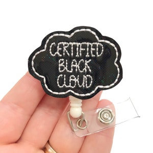 May include: Black cloud-shaped badge holder with the text "CERTIFIED BLACK CLOUD" in white embroidery. The badge holder is attached to a clear plastic retractable badge reel.