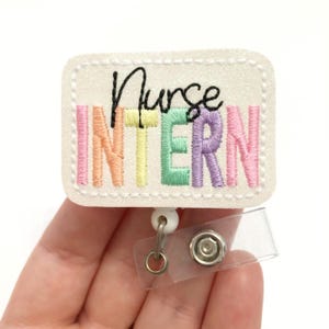 May include: White glitter badge holder with a rainbow embroidered "Nurse Intern" text and a clear plastic badge reel.