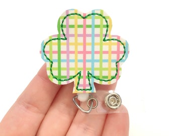 May include: A green shamrock-shaped badge holder with a plaid pattern in pink, yellow, blue, and green. The badge holder has a clear plastic retractable reel.