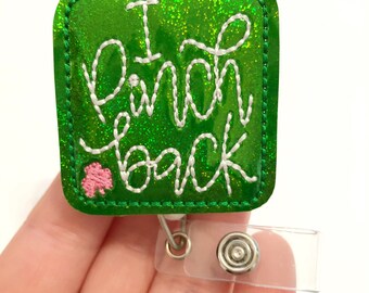 May include: Green glitter badge holder with white stitching and the text "I pinch back" with a pink shamrock. The badge holder has a clear plastic retractable badge reel.