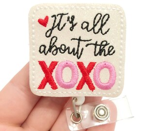 May include: White glitter badge holder with a red heart and the text "It's all about the XOXO" in black and pink lettering.