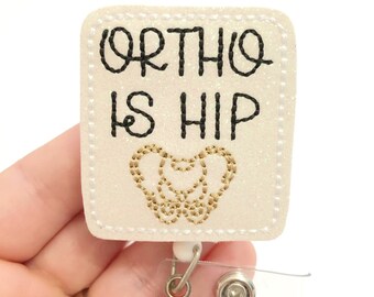 May include: White glitter badge holder with black text that reads "Ortho is Hip" and a gold embroidered hip bone. The badge holder is attached to a clear plastic retractable badge reel.