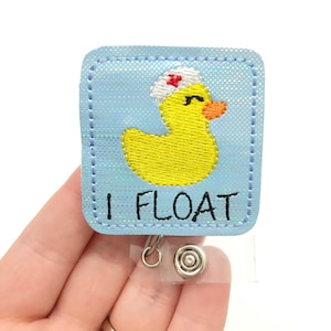 May include: A light blue badge reel with a yellow duck wearing a nurse's cap. The duck has an orange beak and is embroidered on a square background. The text "I FLOAT" is below the duck.
