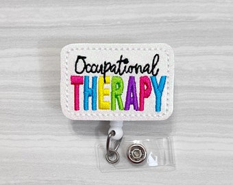 May include: White glitter badge reel with a white rectangular tag that says "Occupational THERAPY" in rainbow colored letters. The letters are embroidered.
