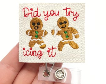 May include: White faux leather badge holder with red embroidery that reads "Did you try icing it". Two gingerbread men are embroidered on the badge holder, one holding a surfboard and the other with a surprised expression.