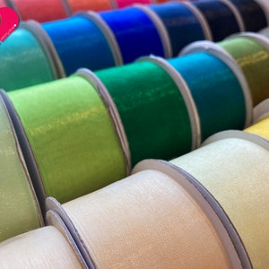 May include: A variety of colorful ribbon spools in different shades of green, blue, yellow, and white. The ribbon is made of a sheer, shimmery fabric.