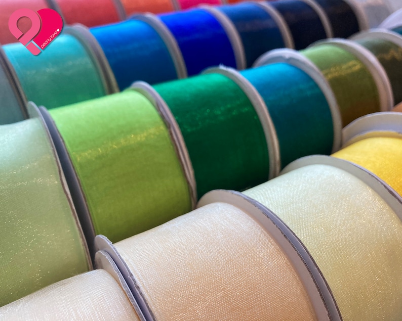 May include: A variety of colorful ribbon spools in different shades of green, blue, yellow, and white. The ribbon is made of a sheer, shimmery fabric.