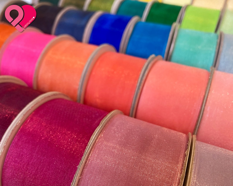 May include: A close-up of spools of colorful sheer ribbon with a glittery finish. The ribbon is arranged in a row, with the colors ranging from pink to purple.
