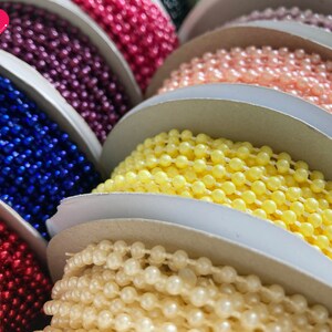 K&ouml;nnte beinhalten: Spulen mit farbigem Perlenbesatz in verschiedenen Farben, darunter Rot, Rosa, Gelb, Wei&szlig;, Blau und Lila.