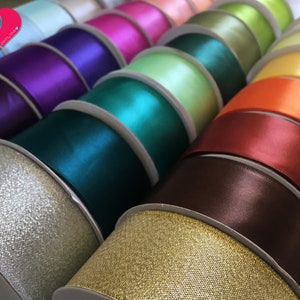 May include: A collection of spools of ribbon in various colors, including teal, purple, gold, and orange. The ribbons have a satin finish and are neatly arranged, showcasing a variety of shades for crafting or decorative purposes.