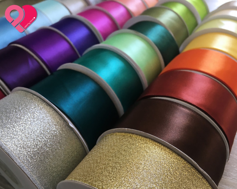 May include: A collection of spools of ribbon in various colors, including teal, purple, gold, and orange. The ribbons have a satin finish and are neatly arranged, showcasing a variety of shades for crafting or decorative purposes.