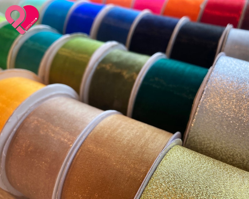 May include: A close-up of a variety of spools of ribbon in different colors and textures, including gold, silver, green, blue, and orange. The ribbons are arranged in a row, with the gold and silver ribbons in the foreground.