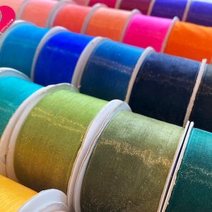 May include: A variety of colorful sheer ribbon rolls with a shimmery finish. The rolls are arranged in a row, with the colors ranging from light blue to dark green.