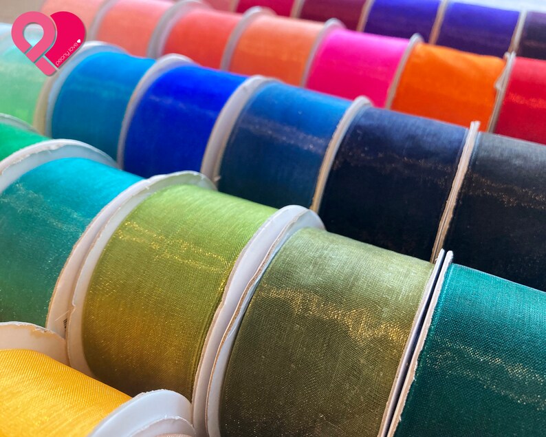 May include: A variety of colorful sheer ribbon rolls with a shimmery finish. The rolls are arranged in a row, with the colors ranging from light blue to dark green.
