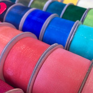 May include: A variety of colorful ribbon spools with a sparkly finish. The ribbon is arranged in a row, with each spool overlapping the next. The colors include pink, blue, teal, green, and yellow.