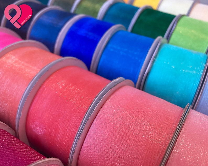 May include: A variety of colorful ribbon spools with a sparkly finish. The ribbon is arranged in a row, with each spool overlapping the next. The colors include pink, blue, teal, green, and yellow.