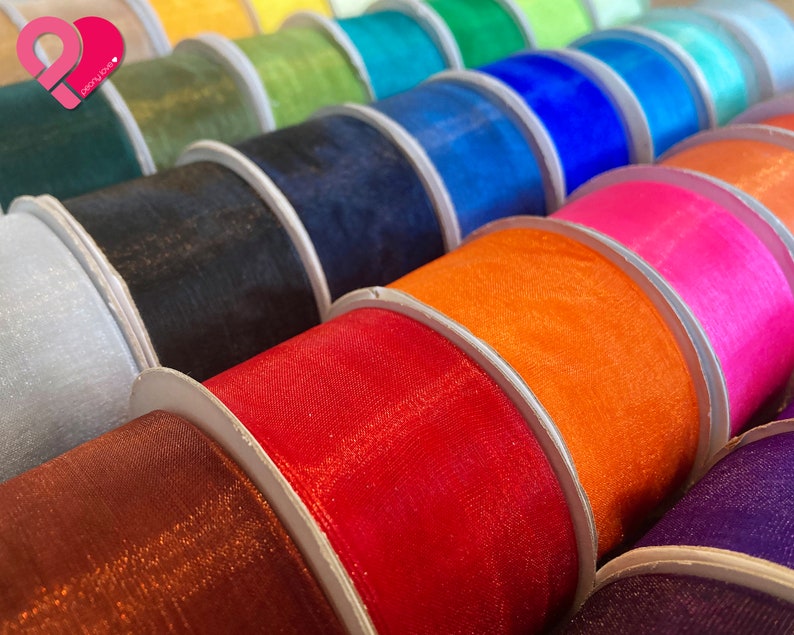 May include: A close-up of spools of colorful sheer ribbon. The ribbon is arranged in a row, with each spool a different color. The colors include red, orange, yellow, green, blue, purple, pink, and white.