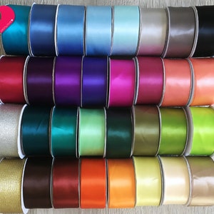 May include: A collection of colorful satin ribbon spools in various shades, including teal, blue, purple, pink, orange, green, and gold. The ribbons are neatly arranged, showcasing their smooth texture and vibrant hues. The image is well-lit, highlighting the sheen of the fabric.
