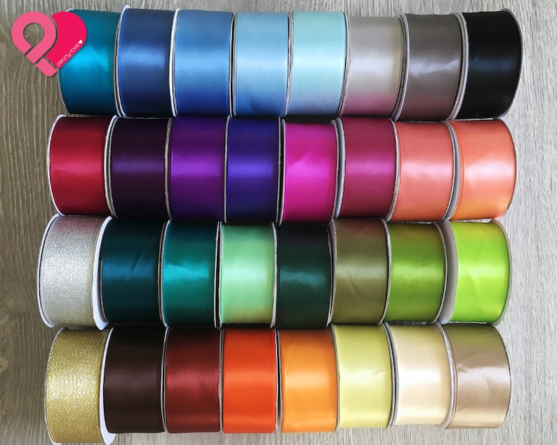 May include: A collection of colorful satin ribbon spools in various shades, including teal, blue, purple, pink, orange, green, and gold. The ribbons are neatly arranged, showcasing their smooth texture and vibrant hues. The image is well-lit, highlighting the sheen of the fabric.